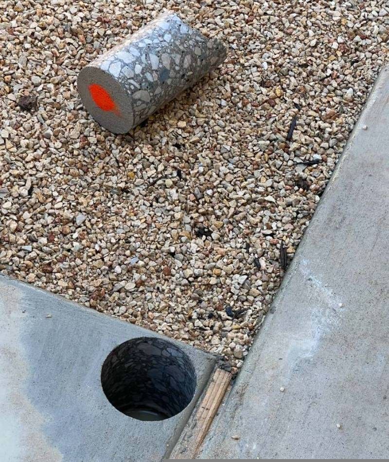 Extracted concrete core sample next to a freshly drilled hole in a slab