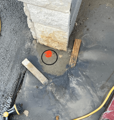 Marked drilling location beside a stone pier at a dumpster enclosure