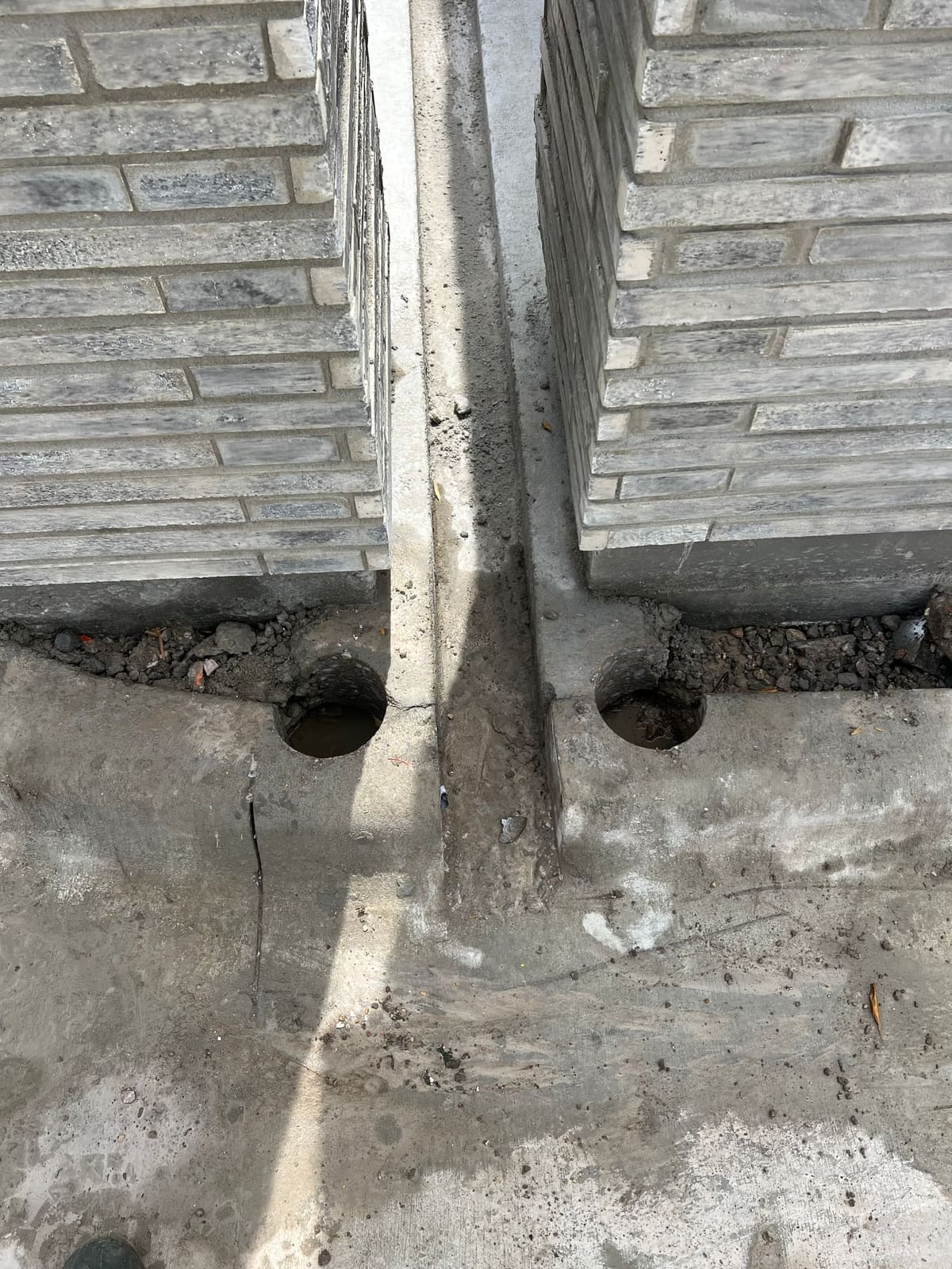 Two core-drilled holes through a poured concrete curb on a job site
