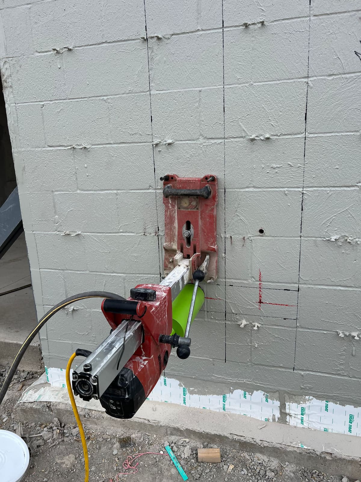 Core drilling rig mounted against a painted concrete block wall for a utility penetration