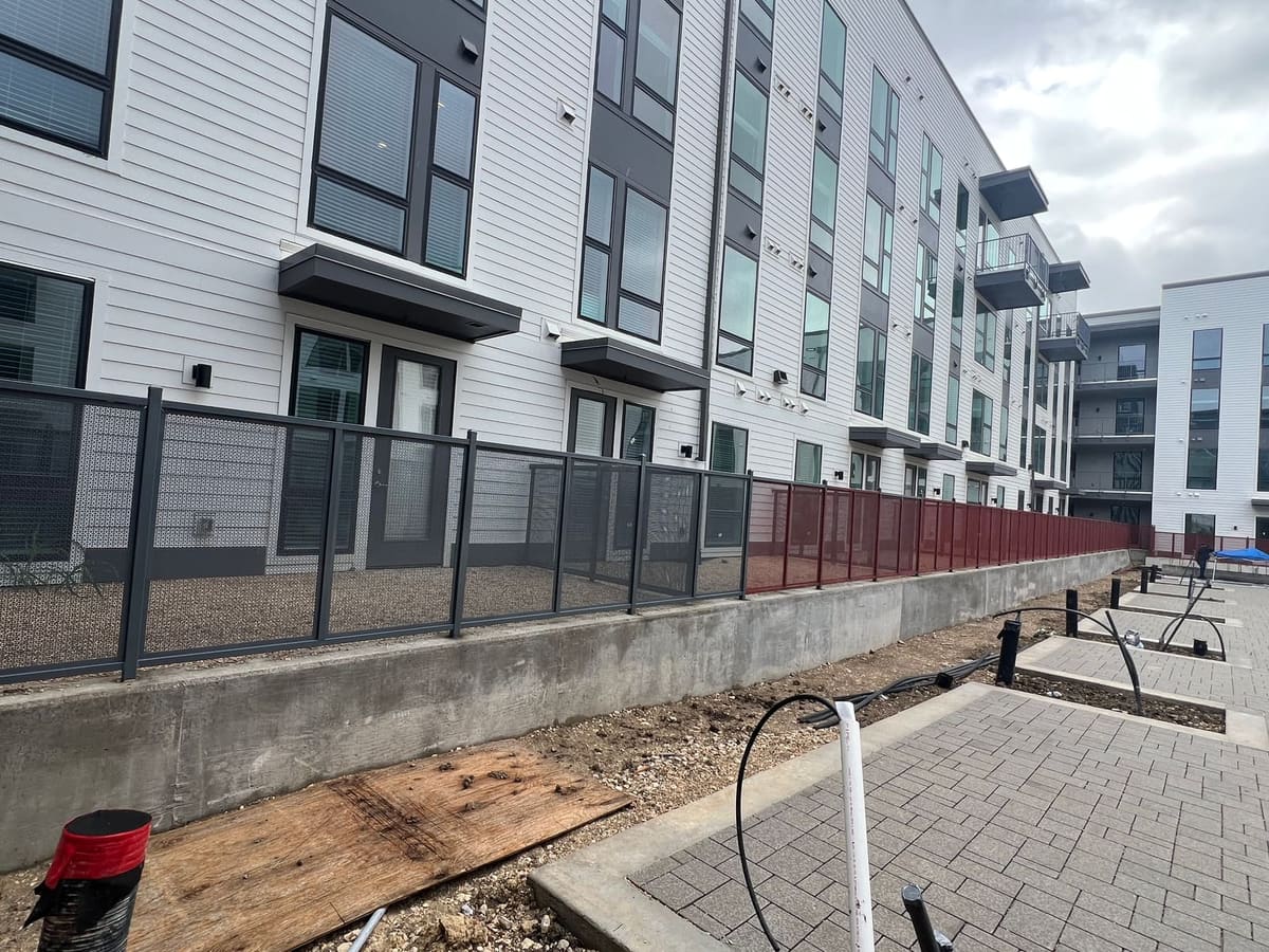 Concrete retaining curb along a courtyard fence line, cored for post anchors